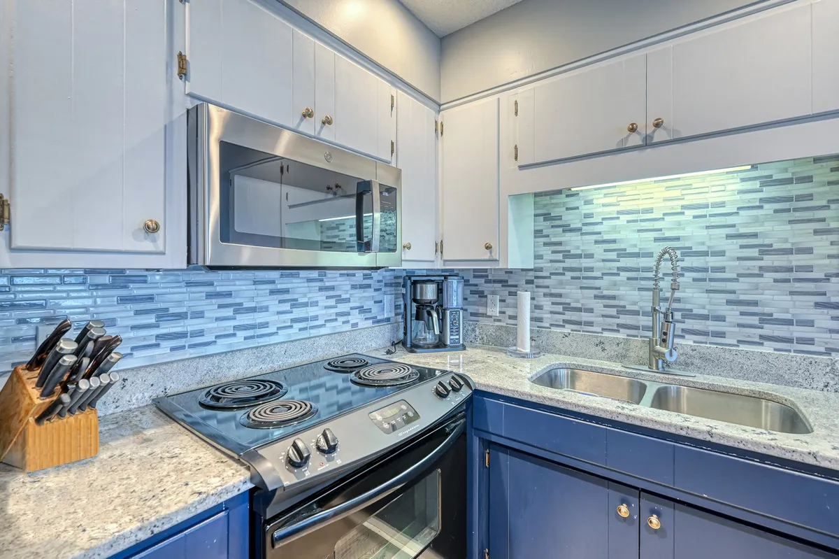 A bright, modern kitchen with stainless steel appliances, sleek granite countertops, and a blue mosaic tile backsplash. Kitchen utensils and essentials are neatly arranged, ready for preparing delicious meals.