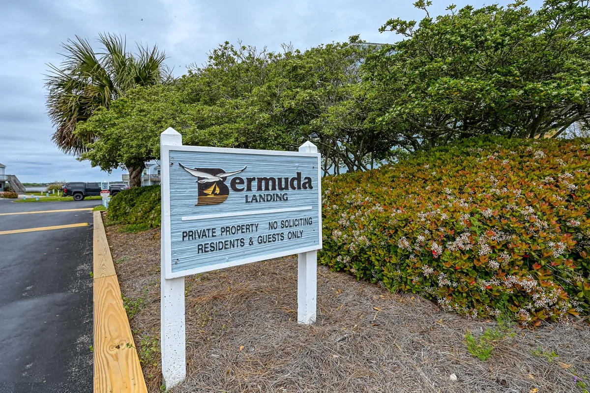 An exterior shot of the Bermuda Landing sign framed by lush greenery, with a paved driveway leading into the community. The image suggests a welcoming and tranquil neighborhood atmosphere, emphasizing entrance and communal spaces.
