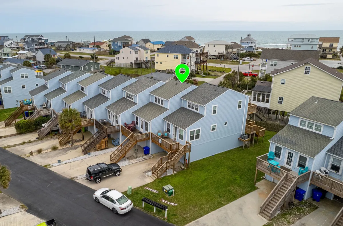 This exterior image showcases brightly colored beach houses with an expansive ocean view in the background. The scene captures the laid-back, inviting atmosphere of a beach community, including the proximity to the shoreline and the potential for outdoor relaxation and family gatherings.