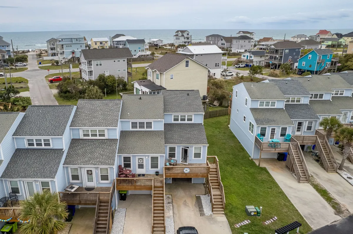 This image presents a beachfront property set among colorful houses with an open green grass area in the foreground. The view suggests a vibrant waterfront community with direct access to both nature and water, ideal for outdoor activities. The presence of the beach, open space, and the proximity to the water strongly evoke opportunities for fishing, kayaking, and exploration.