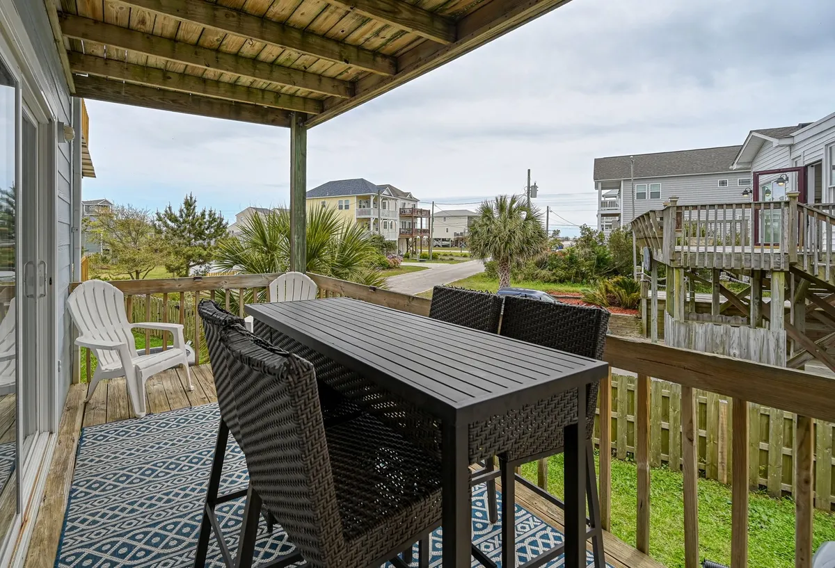 A spacious outdoor dining table with chairs sits on the deck, framed by a railing that offers a glimpse of the surrounding landscape and palm trees. The mood is casual and inviting, perfect for al fresco dinners, stargazing, or gathering with loved ones to savor the sweeping sound views.