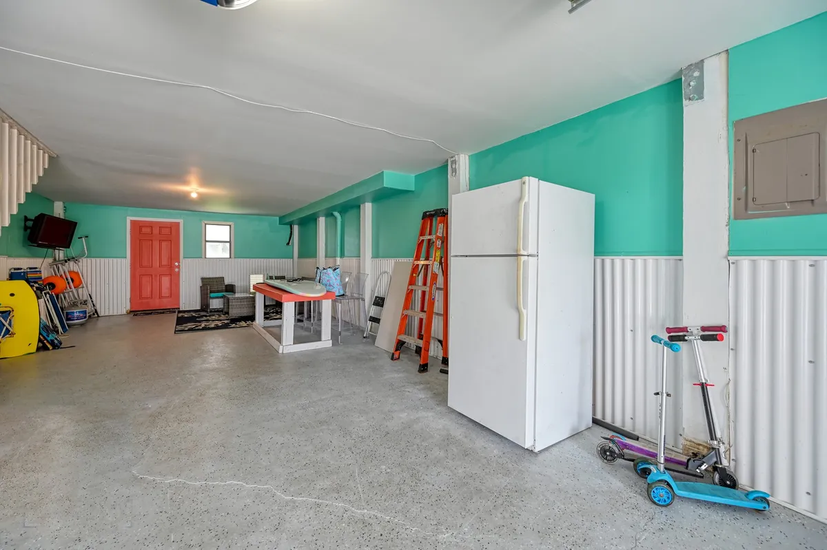 A colorful, cheerful interior scene with brightly painted walls, a refrigerator, table with chairs, a ladder, and visible outdoor equipment. The space embodies flexibility and utility, offering room for storage, extra cold storage with the fridge, and multipurpose use for family activities.