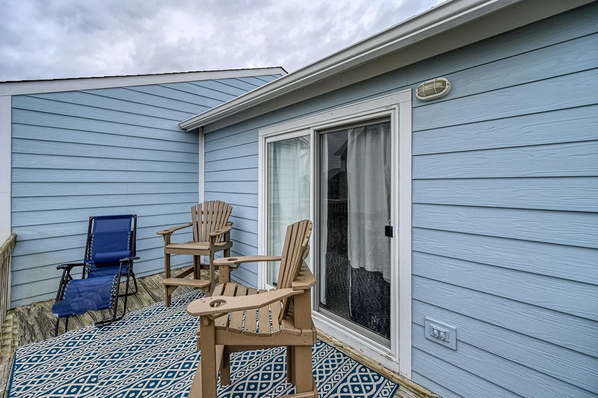 A serene exterior scene showing wooden chairs and a decorative rug on a patio, with a sliding glass door in the background. The arrangement suggests a calm setting perfect for relaxing after outdoor adventures or for observing the surrounding natural beauty and wildlife.