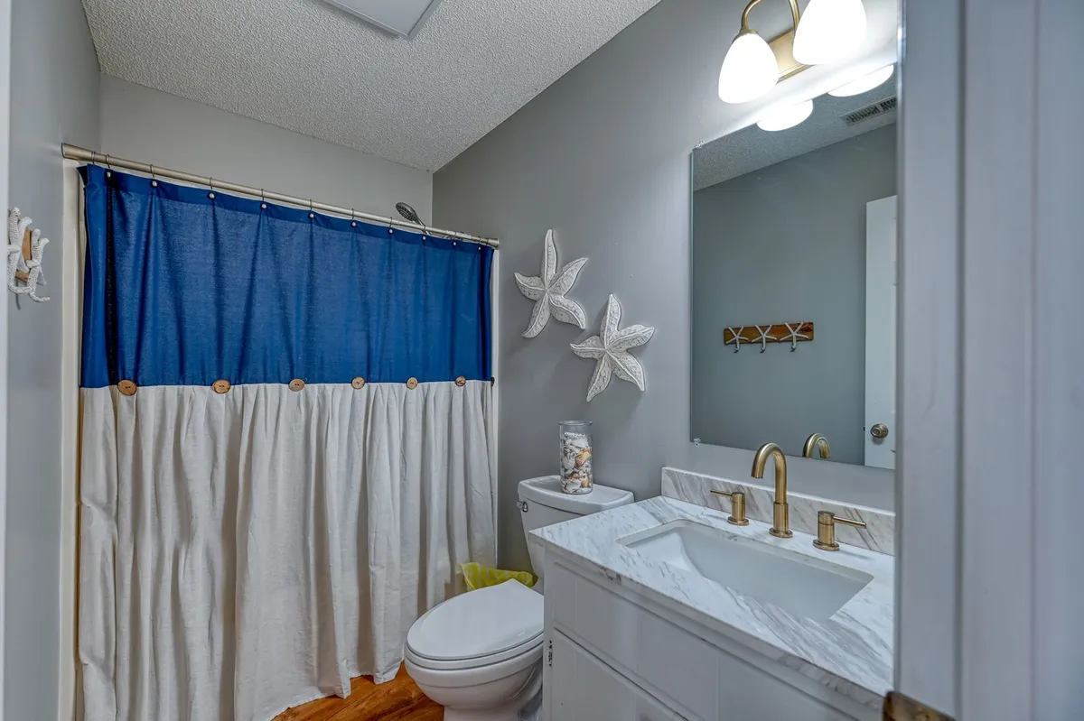 A spa-like bathroom with a blue shower curtain, gold fixtures, starfish wall decor, a marble countertop, and warm wooden flooring. The space feels inviting and serene, ideal for unwinding after a long day or starting the morning refreshed.